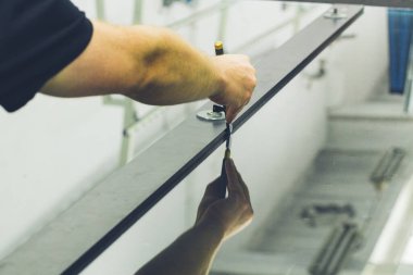 Cam fabrikasındaki bir çalışan özel aletlerin yardımıyla büyük bir cam levha kesiyor. 
