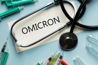 Omicron, Coronavirüs 'ün yeni bir türü şırınga ve tıbbi stetoskop çevresindeki mutasyonun adı yazılı bir kart. 