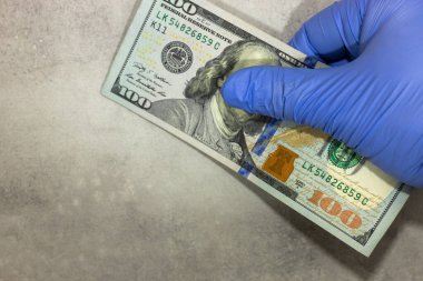 Bir laboratuvar eldiveninde bulunan 100 Amerikan Doları 'nın banknotu, metinler için yer, salgın covid 19 maliyetleri ve dünya ekonomisinde yeni virüs mutasyonu. 