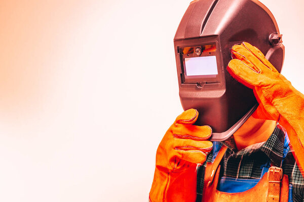 Welder in a protective suit, gloves, taking off his welding mask, Close-up, Fire colors