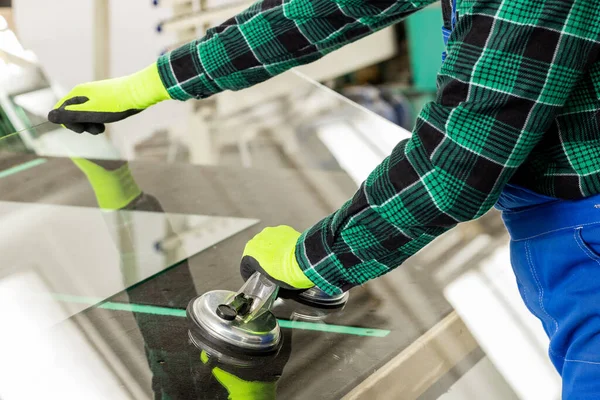 A specialist in a glass company removes a large pane of glass from the table using a specialized glass suction cup, a glazier who does the work