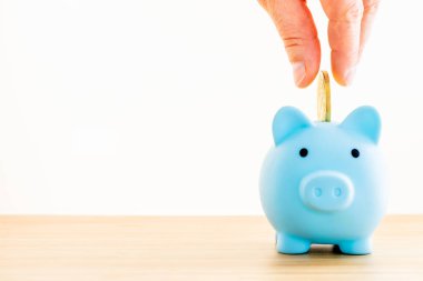 a blue piggy bank on a white background, hand tossing a gold coin inside