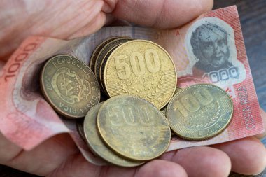 Kosta Rika parası, bir avuç dolusu parlak para ve elinde duran bin kolon banknotu.