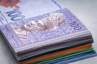 Bir tomar Malezya parası, gri bir masanın üstünde ringitler, üstünde 100 banknot, ekonomi ve iş konsepti.