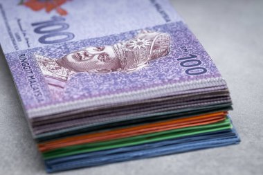 Bir tomar Malezya parası, gri bir masanın üstünde ringitler, üstünde 100 banknot, ekonomi ve iş konsepti.