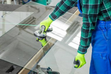 Cam şirketinde çalışan bir uzman, özel cam vakum kabı kullanarak masadan büyük bir cam levhayı kaldırır.  