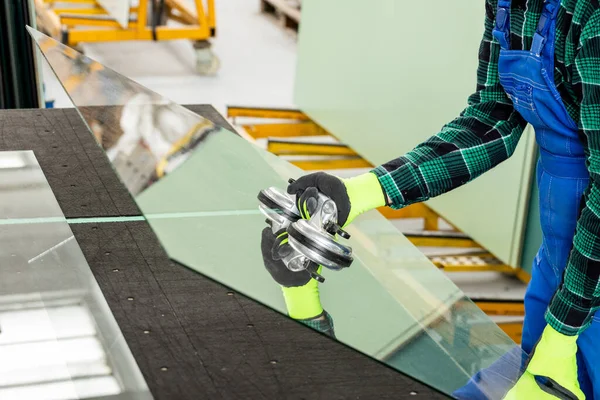 A specialist in a glass company removes a large pane of glass from the table using a specialized glass suction cup, a glazier who does the work