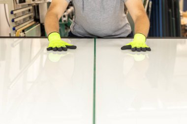 Camcı, profesyonel bir masadaki cam fabrikasında beyaz bir camı keser ve kırar.