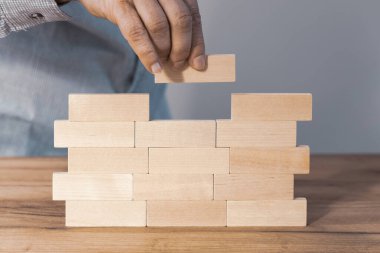 Creating a stable foundation for the company's operations, Business development based on solid foundations Creative concept, Entrepreneur builds a wall of wooden blocks, Building customer trust