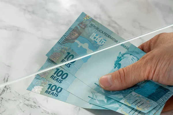 Brazilian money file, banknotes of 100 reais, Passing through a bank window, Creative concept, Paying bills, Customer service at the checkout, currency deposit