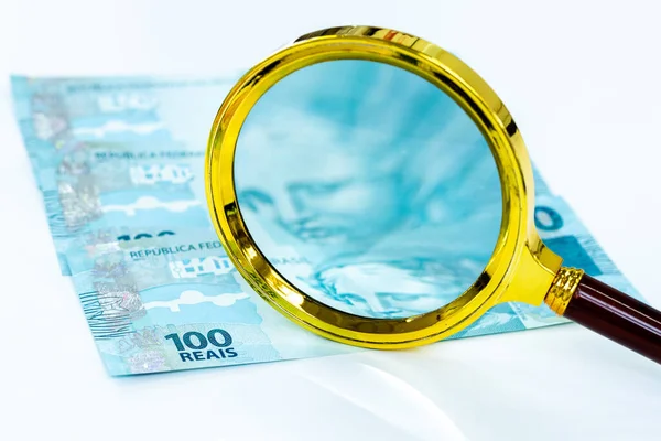 Brezilya parası, düz hesap, 100 reais banknot, büyüteç, beyaz zemin, iş ve finans konsepti, piyasa ve enflasyon gözlemi, para birimi istikrarı