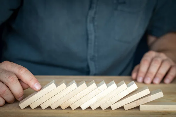 Unsuccessful business transaction, Economic collapse, Market crisis, Creative concept, Bad company management, A businessman stands over wooden blocks overturned like dominoes