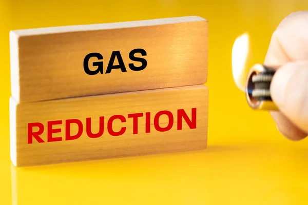 Gas reduction, written on a wooden block, yellow background, a burning lighter in hand, the concept of the european energy crisis