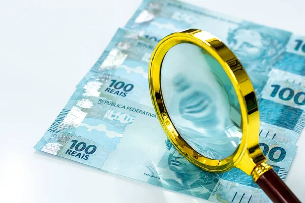 Brezilya parası, düz hesap, 100 reais banknot, büyüteç, beyaz zemin, iş ve finans konsepti, piyasa ve enflasyon gözlemi, para birimi istikrarı