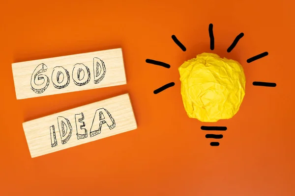 Good Idea, written in youth style on wooden blocks, Beautiful orange background, Crumpled ball of paper in the form of a burning light bulb, Concept, Brainstorming, Innovative ideas,