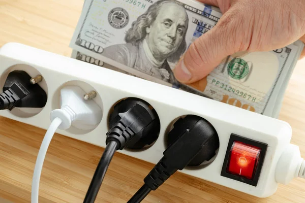 Increases in electricity prices in the United States, Energy concept, Power strip with plugs plugged in and a large bundle of dollars in hand, Increase in energy prices for households and industry