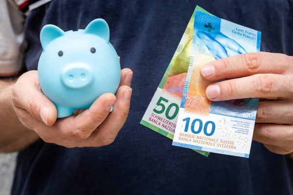 Swiss francs and a small piggy bank held in the hands, saving concept