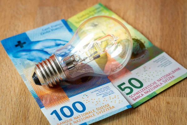 Swiss money 150 francs and a light bulb, concept of rising energy and electricity prices in Switzerland