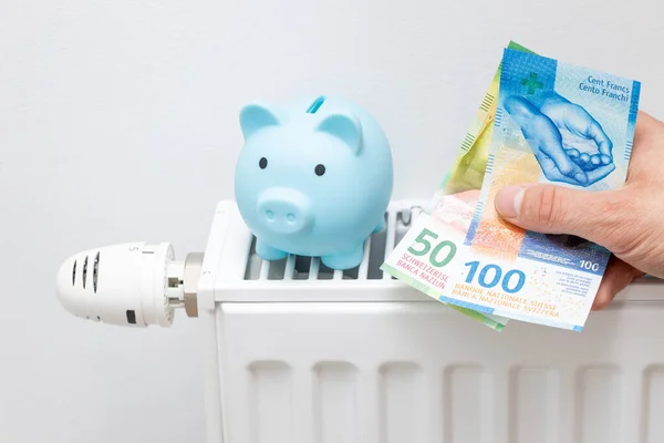 Prices for heating apartments in winter, Increase in energy prices in Switzerland, Heater and Swiss Francs held in the hand and a piggy bank for money