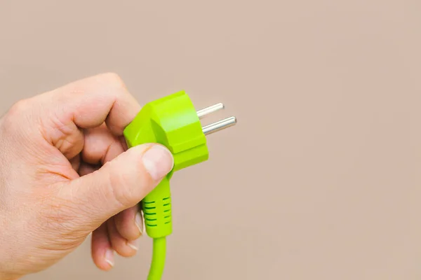 Green plug in hand, Latte-colored background, The concept of using green energy and the use of modern methods of obtaining energy in harmony with the natural environment