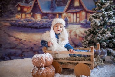 Beyaz şapkalı ve botlu bir çocuk kış köyündeki yapay bir ormanın arka planında.