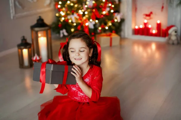 Dziecko trzyma Boże Narodzenie w swoich rękach. prezent na tle malowane drzewo nowy rok domu — Zdjęcie stockowe