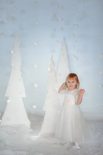Cute girl in white Princess costume between white artificial glowing Christmas trees