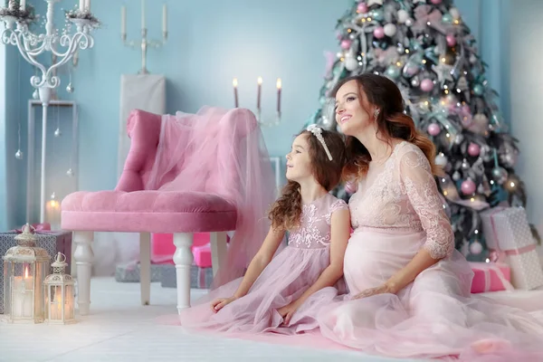 Maman dans une robe élégante avec sa fille assise sur le sol dans la pièce de la maison près du sapin de Noël — Photo