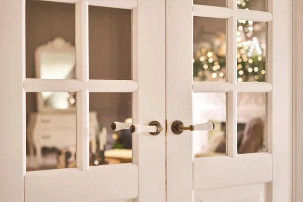 Όμορφο μοντέρνο πόμολο. Χριστουγεννιάτικα φώτα στο φόντο. Ανοιχτή, ξύλινη μπροστινή πόρτα από το εσωτερικό ενός υπερυψωμένου σπιτιού με παράθυρα. — Φωτογραφία Αρχείου