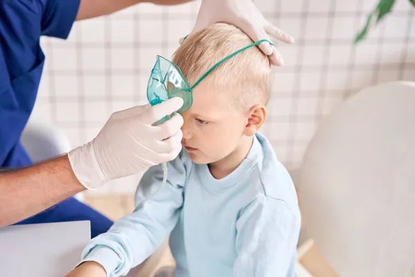 Ein Kinderarzt diagnostiziert Lungenerkrankungen und behandelt sie. Atmen Sie das Medikament durch einen Vernebler-Inhalator ein. Porträt eines entzückenden kleinen Jungen beim Arztbesuch. — Stockfoto