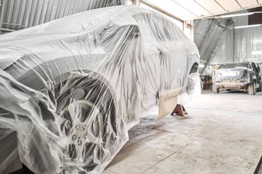 Garaj boyama servisi. Arabanın bir kısmı fünyeyle kaplanmış. Araç koruyucu kağıtlarla kaplı. Araba kaportası tamiri kazadan sonra boyamadan önce astar zımparalamayla yapılıyor..