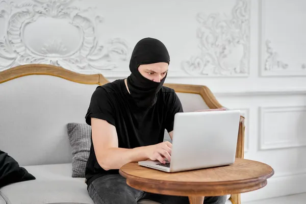 Porträtt av oigenkännliga unga hacker i svart mask med bärbar dator. Begreppet cybersäkerhet och dataskydd — Stockfoto
