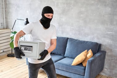 Siyah maskeli bir hırsız elektronik kilidi olan modern metal kasayı çalıyor. Ev hırsızlığı para ve belge konsepti.