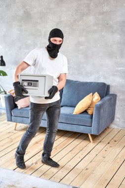 Siyah maskeli bir hırsız elektronik kilidi olan modern metal kasayı çalıyor. Ev hırsızlığı para ve belge konsepti.