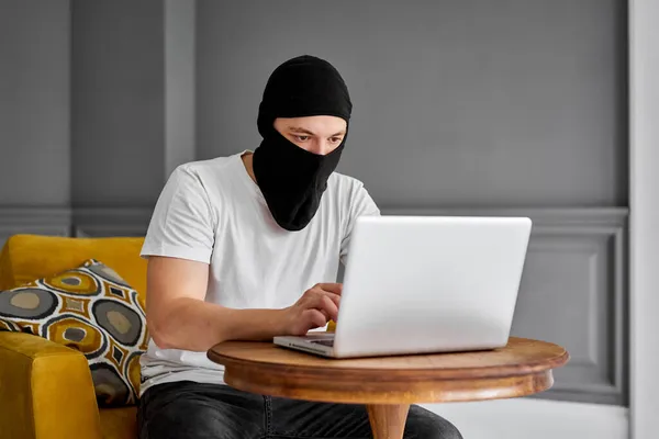 Портрет невпізнаваного молодого хакера в чорній масці з використанням ноутбука. Концепція кібербезпеки та захисту даних — стокове фото