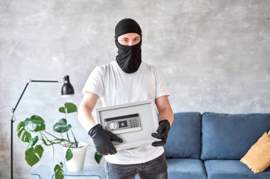 Siyah maskeli bir hırsız elektronik kilidi olan modern metal kasayı çalıyor. Ev hırsızlığı para ve belge konsepti.