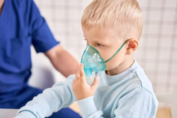 A gyermekorvos diagnosztizálja a tüdőbetegséget, és biztosítja a kezelést. Lélegezze be a gyógyszert porlasztó inhalátorral. Aranyos kisfiúról készült portré, aki orvoshoz megy.. — Stock Fotó