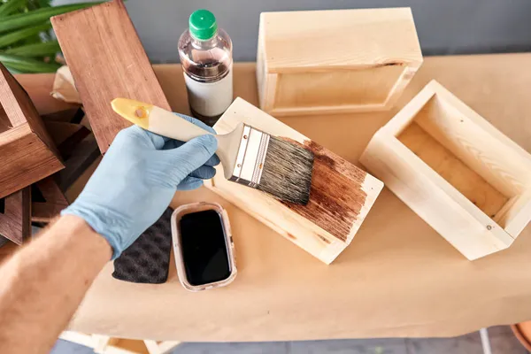 Hombre carpintero barnizado caja de madera para flores con pincel en su taller de carpintería pequeña empresa. En su trabajo, ¿utiliza manchas o conservantes de madera para mostrar el patrón de madera . — Foto de Stock