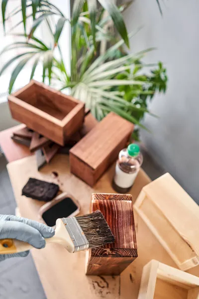 男人木匠在她的小作坊里用刷子把木箱装饰成鲜花.在你的作品中，你是否使用污渍或木材防腐剂来展示木材图案？. — 图库照片