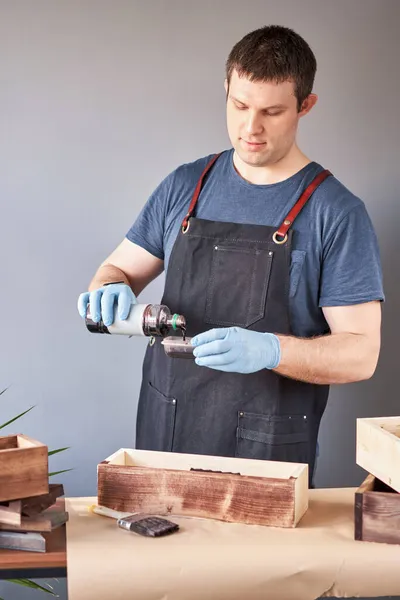 Man timmerman lakken houten krat met borstel in haar kleine bedrijf. Gebruik je in je werk vlekken of houtconserveringsmiddelen om het houtpatroon weer te geven?. — Stockfoto