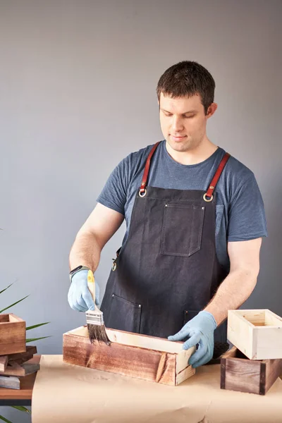 Hombre carpintero barnizado caja de madera con cepillo en su pequeño negocio. En su trabajo, ¿utiliza manchas o conservantes de madera para mostrar el patrón de madera. — Foto de Stock