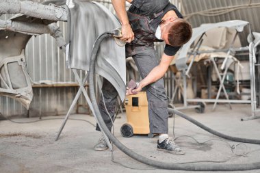 Araba parçalarının zımparalanması. Tamirci öğütücü bir aletle çalışıyor. Araba boyama servisi. Kazadan sonra araba bölümü tamir ediliyor..