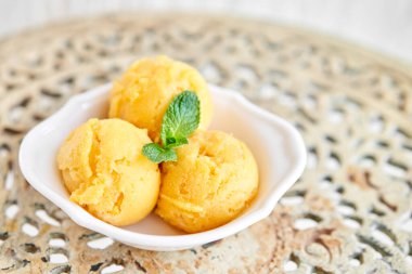 Naneli mango dondurması. Eski bir masada beyaz bir kasede üç top. şerbet