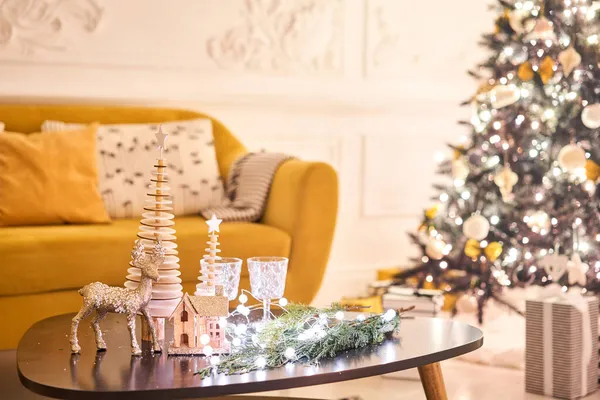 Dekorowany stół we wnętrzu świąt Bożego Narodzenia. Choinka. Zbliżenie mały dom, szyszki, girlanda, i inne zabawki choinkowe. światło z girlandy — Zdjęcie stockowe