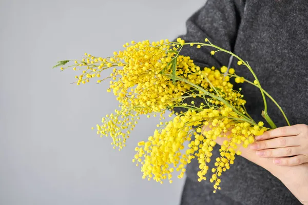 女人手里拿着一丛丛美丽的油烟花和妖怪。窗边的白桌子上挂着黄色的、阳光灿烂的花.送新鲜切花。欧洲花店. — 图库照片