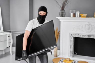 Modern pahalı televizyonu çalan siyah kar maskeli bir hırsız. Maskeli yüz. Hırsız evden televizyon çalıyor.
