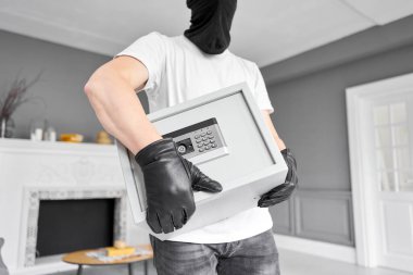 Siyah maskeli bir hırsız elektronik kilidi olan modern metal kasayı çalıyor. Ev hırsızlığı para ve belge konsepti.