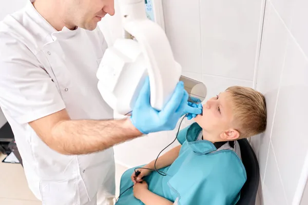 Radiógrafo llevando radiografía de dientes a un niño usando una máquina de rayos X digital en una clínica dental pediátrica. Dentista prepara niño para la imagen de rayos X dental en clínica dental. — Foto de Stock