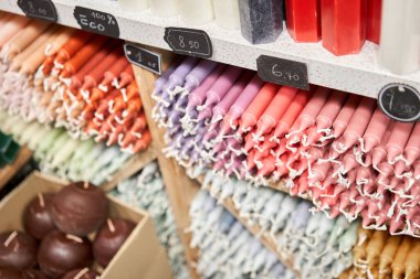 Many multicolored colorful paraffin stick Pastel colors candles arranged in shelves lying on shelter and sorted by color in a household candle shop store market