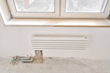 İnşaat halindeki yeni bir apartmanın beyaz radyatörüne bağlı ısıtma boruları. Su tesisatçısı olarak çalış. Beyaz duvarda su ısıtıcısı monte et.,
